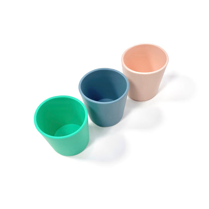 A collection of silicone children’s cups, available in peachy pink, ocean blue and seafoam green. The cups are shown lined up diagonally.