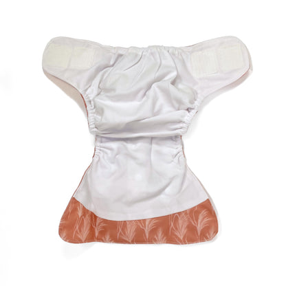 An adjustable reusable nappy for babies and toddlers, featuring a sunset dune design, with images of grasses on a reddish-brown background. View shows the inside fabric of the nappy.
