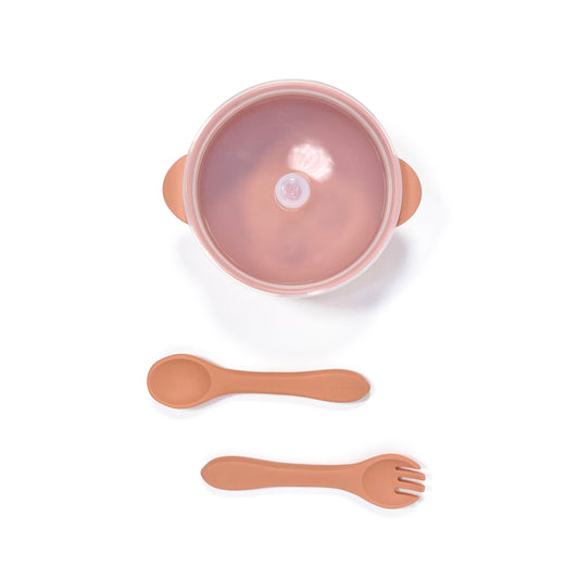 A sunset orange silicone children’s feeding set, including silicone bowl with lid and matching silicone cutlery. Image shows the bowl and cutlery from above, with lid attached.