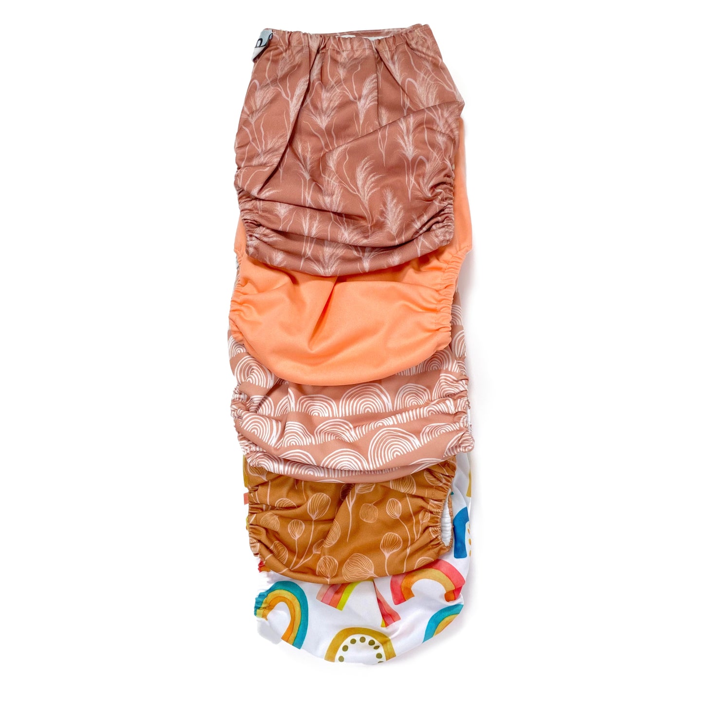 A set of five reusable nappies, made from 100% recycled polyester. The included nappies are: Bright Rainbow, Copper Bloom, Peach Rainbow, Cute Coral and Sunset Dune. View shows all five nappies back facing, in a vertical line.