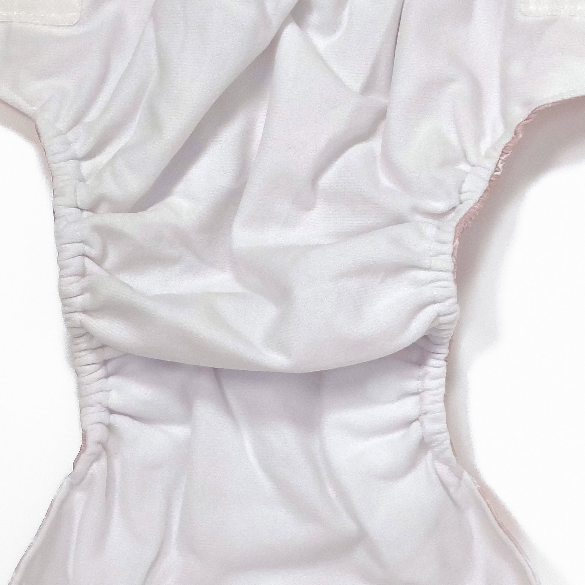 An adjustable reusable nappy for babies and toddlers, featuring a floral lilac design, with floral images on a lilac background. Image shows a zoomed in view of the nappy fabric lining.