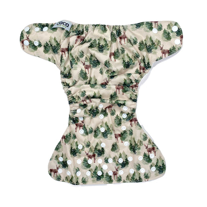 An adjustable reusable nappy for babies and toddlers, featuring a winter forest design with images of deer and pine trees on a cream background. View shows the full outside pattern of the nappy, with fastenings open.