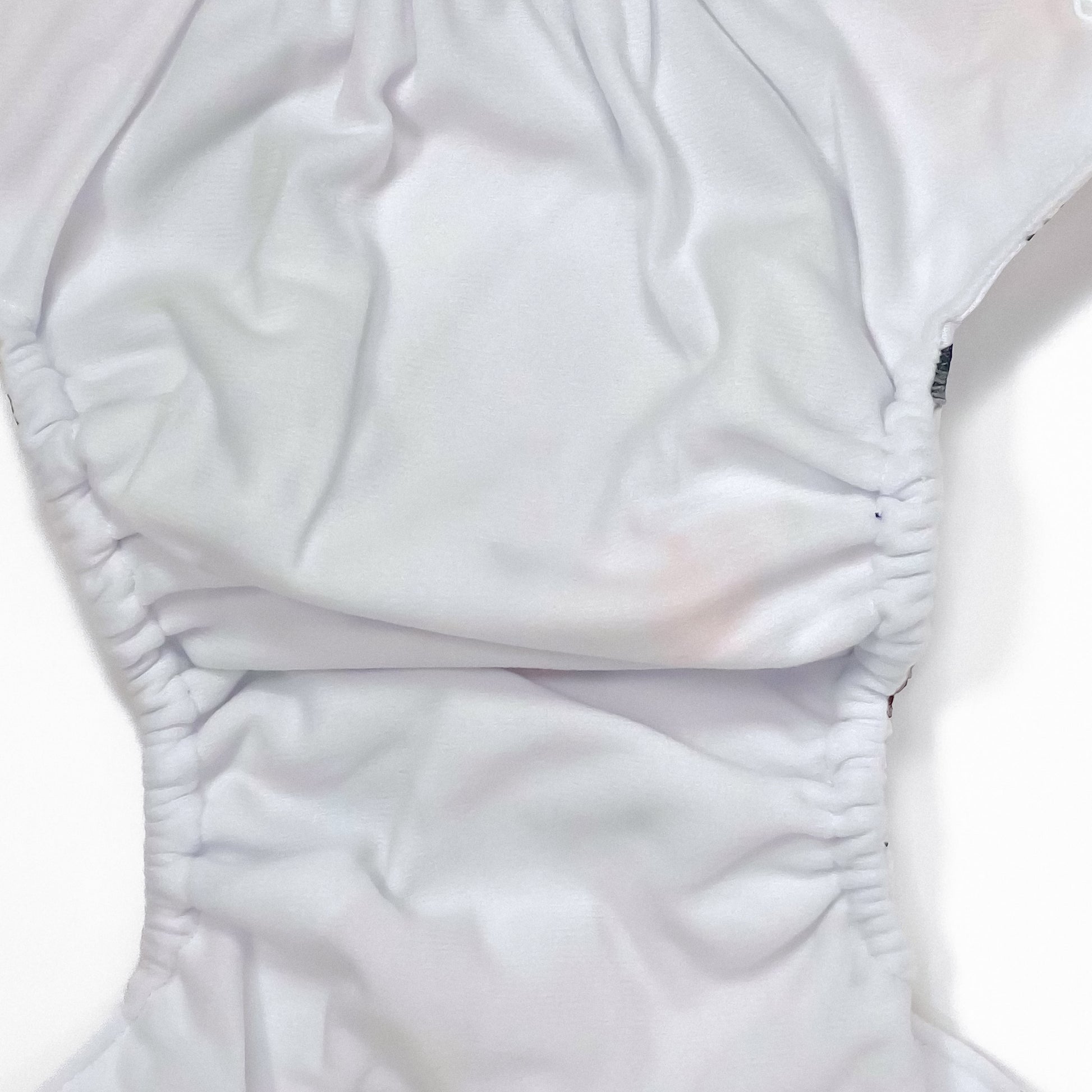 An adjustable reusable nappy for babies and toddlers, featuring a woodland animal design, with images of various woodland animals on a white background. Image shows a zoomed in view of the nappy fabric lining.