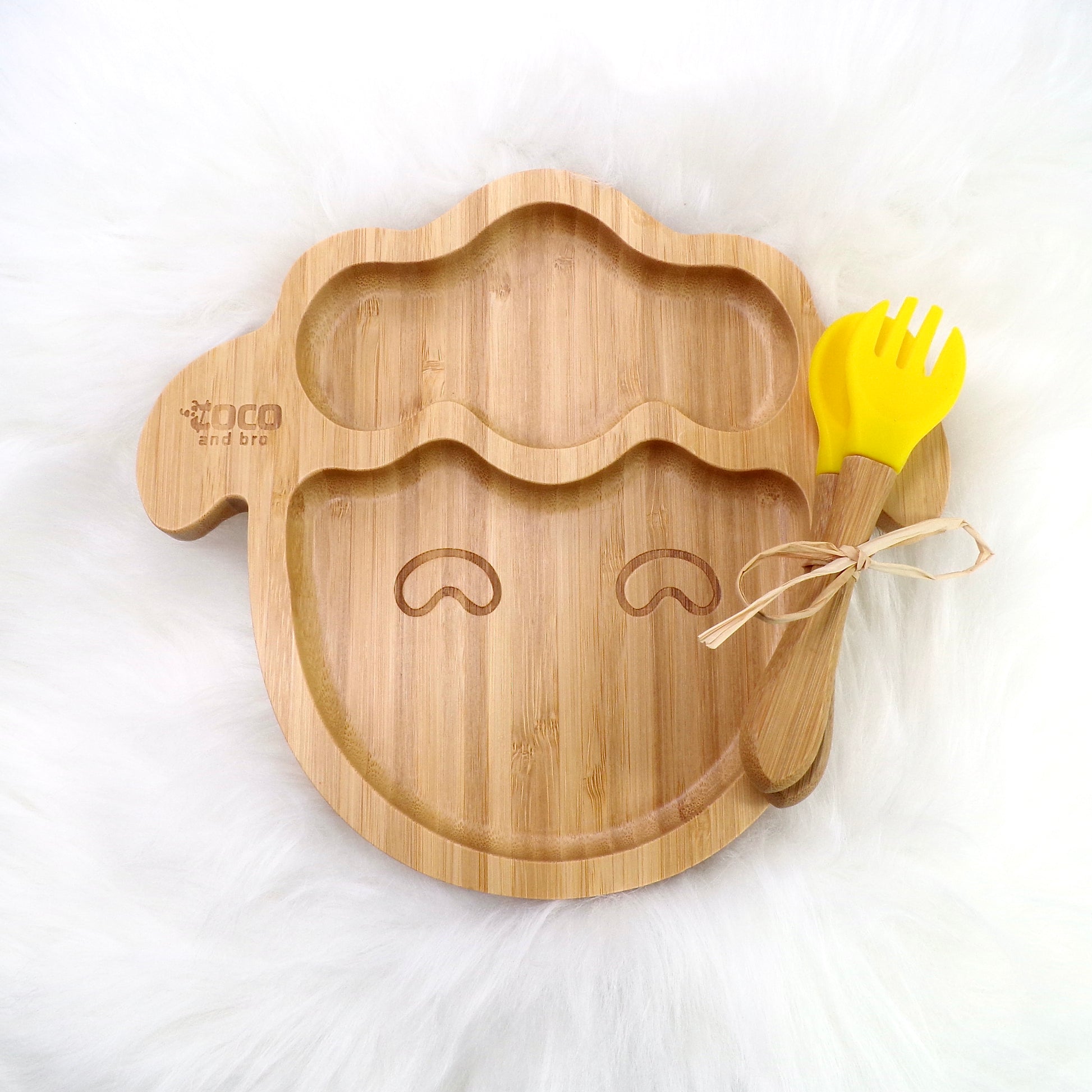 A children's bamboo section plate with a lamb design, yellow colour silicone suction ring and matching yellow bamboo and silicone cutlery. Front view.
