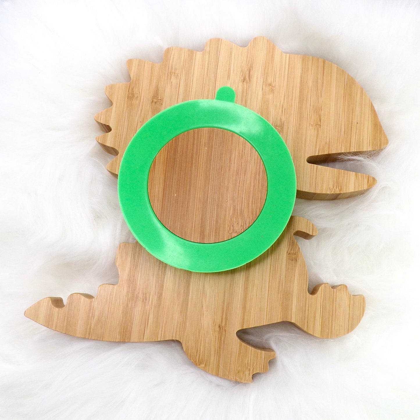 A bamboo children’s plate, with multiple food sections, in a dinosaur design. The bamboo plate features a green silicone suction ring at the back, and includes bamboo fork and spoon utensils in matching colours. Back view.