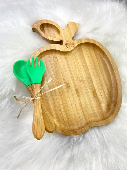 A bamboo children’s plate, with multiple food sections, in an apple design. The bamboo plate features a green silicone suction ring at the back, and includes bamboo fork and spoon utensils in matching colours. Front view.