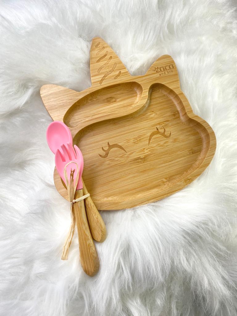 A bamboo children’s plate, with multiple food sections, in a unicorn design. The bamboo plate features a pink silicone suction ring at the back, and includes bamboo fork and spoon utensils in matching colours. Front view.