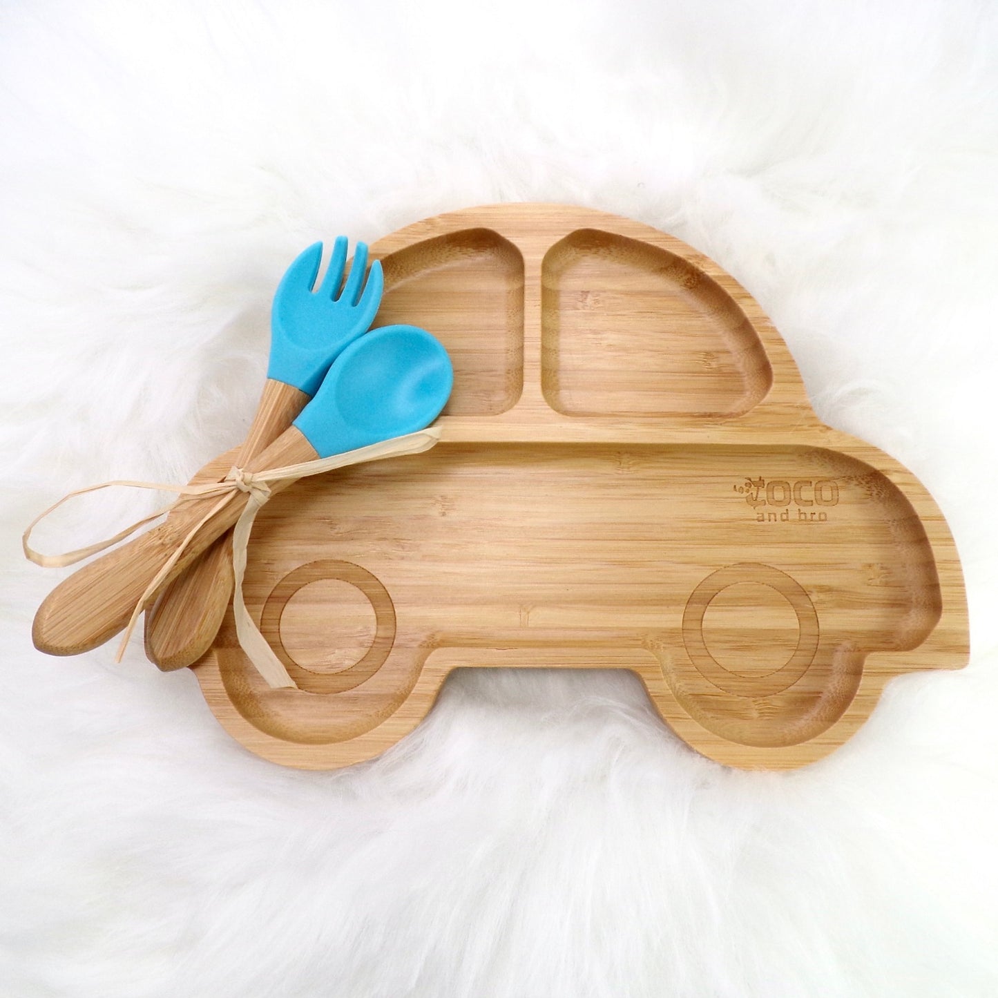 A bamboo children’s plate, with multiple food sections, in a car design. The bamboo plate features a blue silicone suction ring at the back, and includes bamboo fork and spoon utensils in matching colours. Front view.