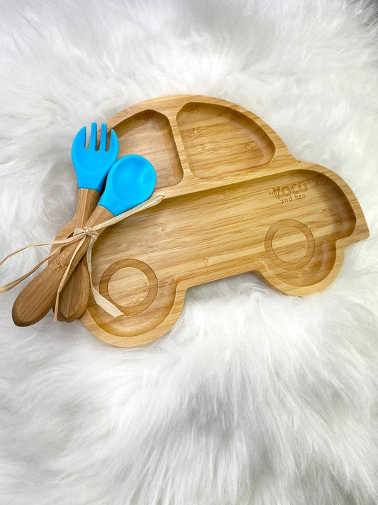 A bamboo children’s plate, with multiple food sections, in a car design. The bamboo plate features a blue silicone suction ring at the back, and includes bamboo fork and spoon utensils in matching colours. Front view.